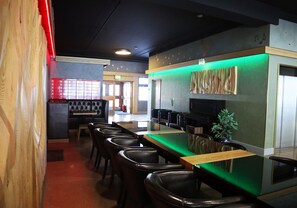 A restaurant with a long counter, multiple chairs, and a green-lit wall decoration. - Eidsvoll Express Hotel (Eidsvoll)