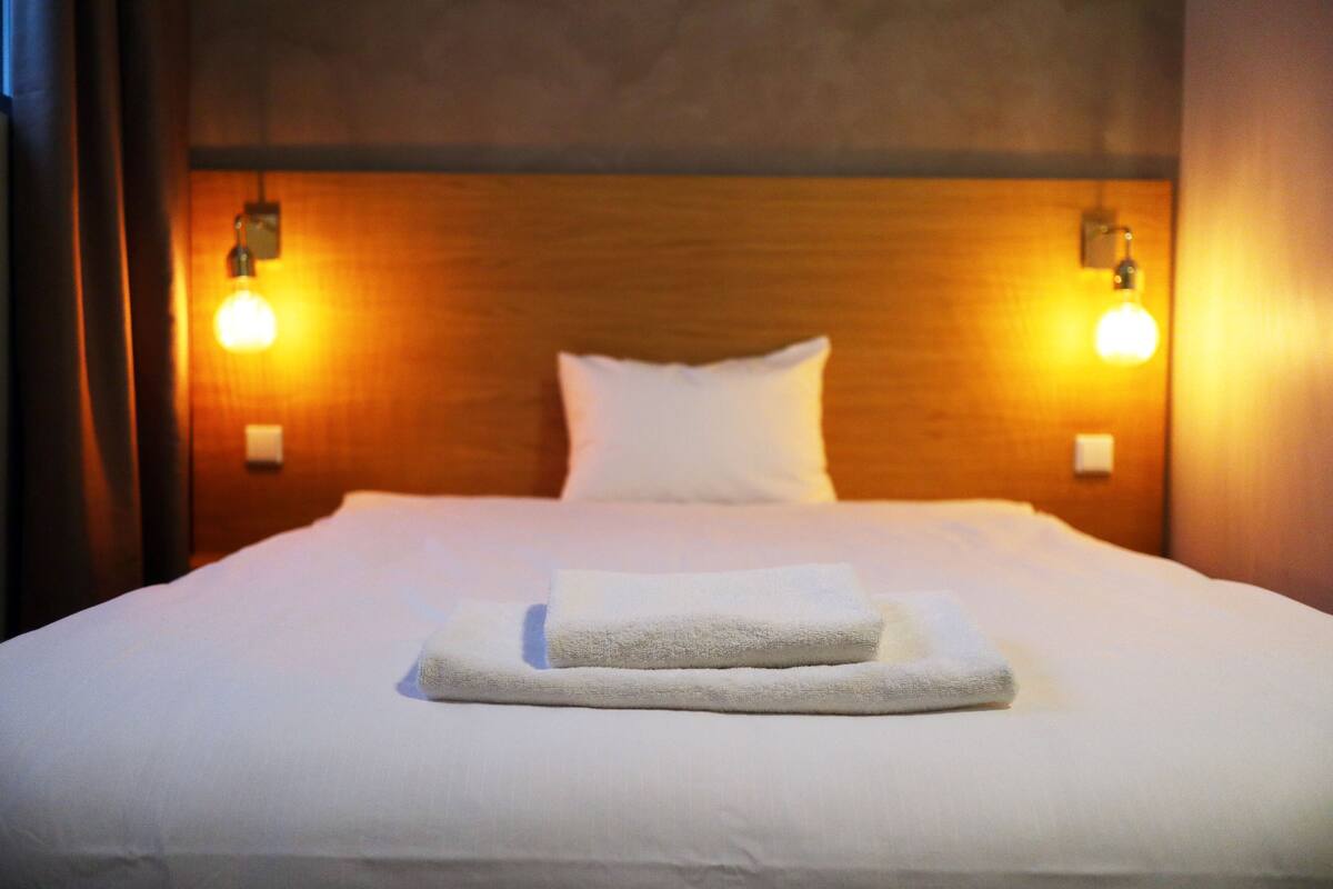 Cama bem arrumada com lençóis brancos e duas toalhas dobradas.