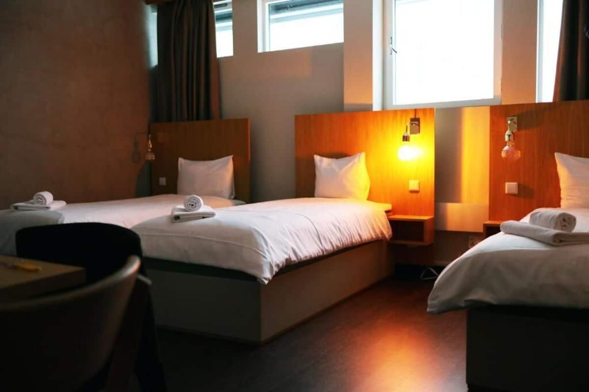 Quarto de hotel com duas camas de solteiro, uma escrivaninha e uma cadeira.