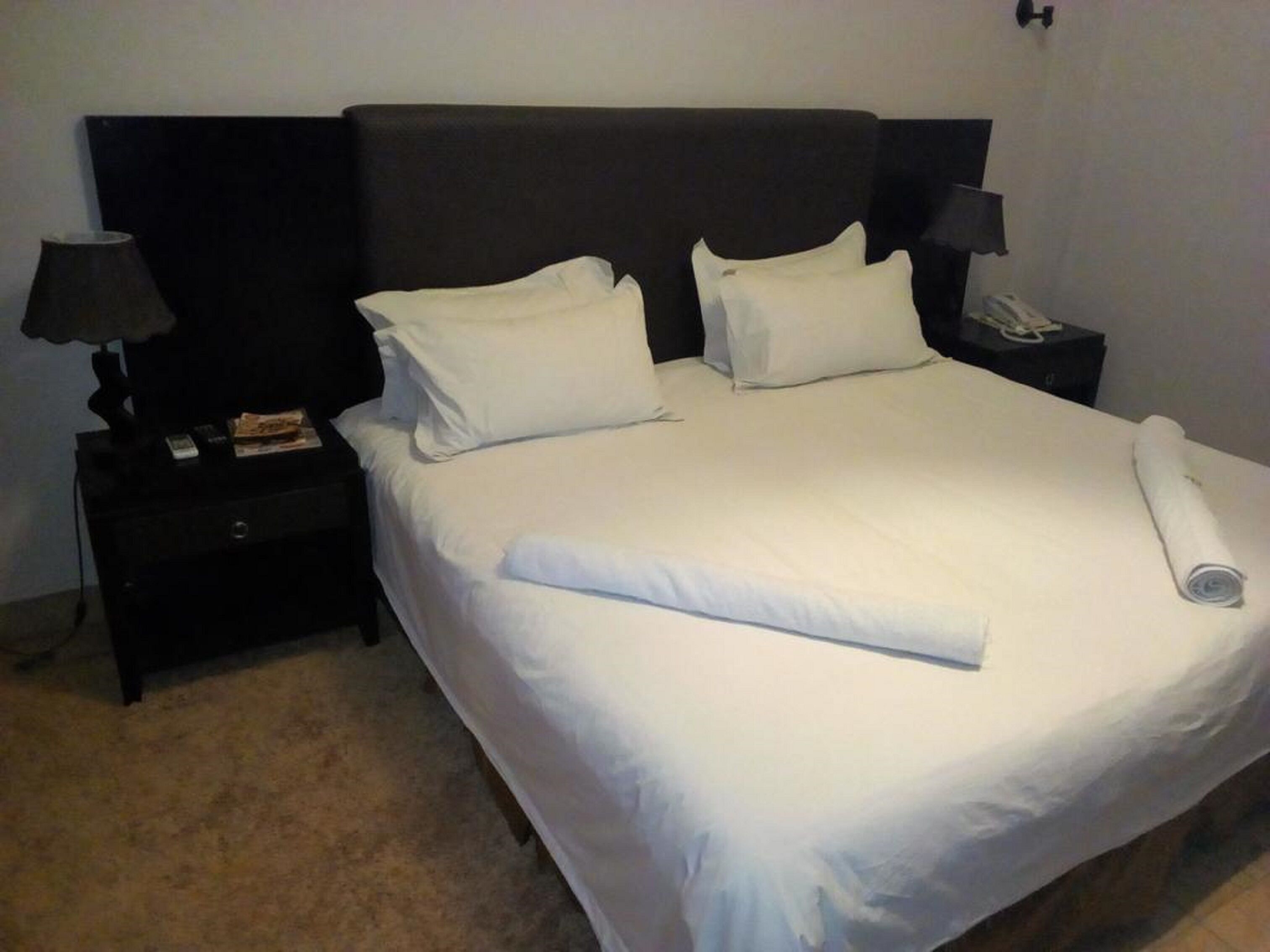 Ein ordentlich gemachtes Bett mit weißen Leinen und Kissen, ein dunkles Kopfteil, ein Nachttisch mit Lampe und Telefon.