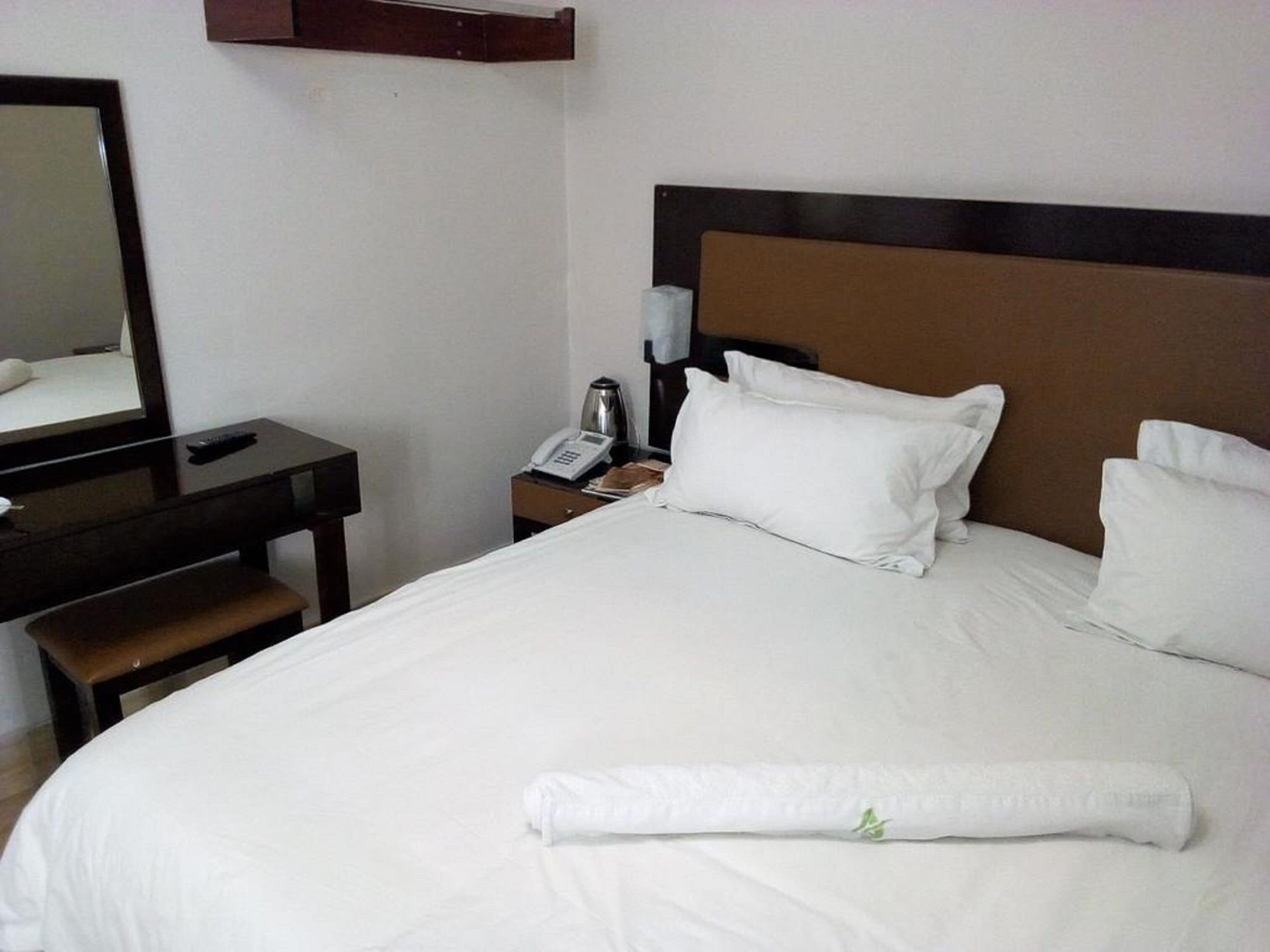 Une chambre d’hôtel avec un grand lit, un bureau, une chaise, un téléphone et un miroir.