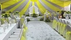 Un salón de banquetes con una larga mesa dispuesta para un evento formal, cubierta con tela amarilla.