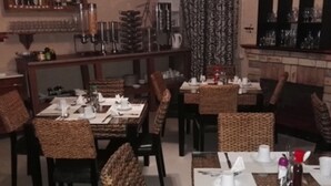 Restaurante con varias mesas dispuestas para comer, con sillas de mimbre y una zona de bar con botellas y vasos.