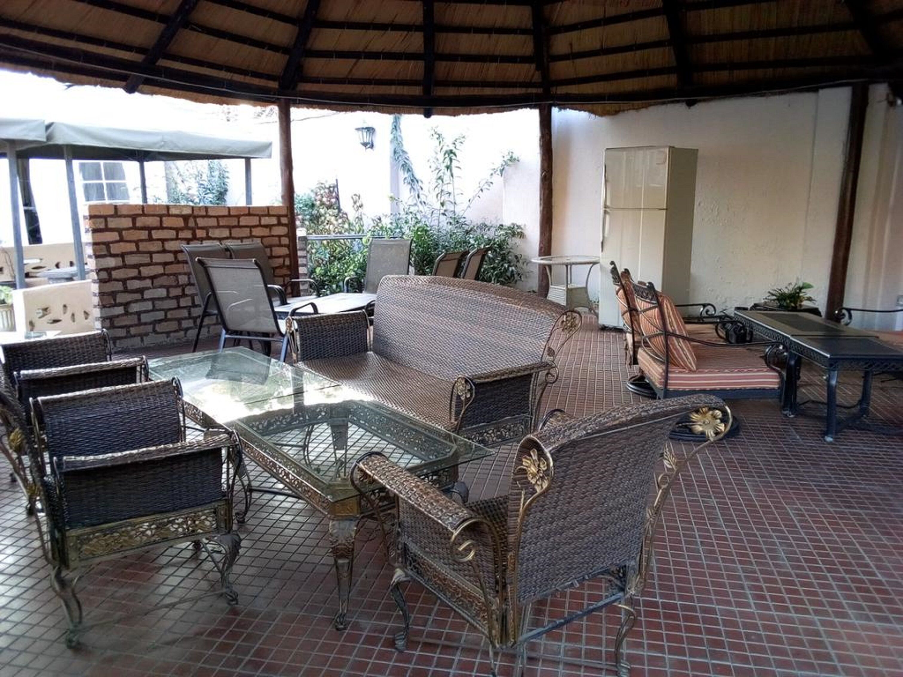 An outdoor patio area with wicker furniture, a glass-top table, and a brick wall.
