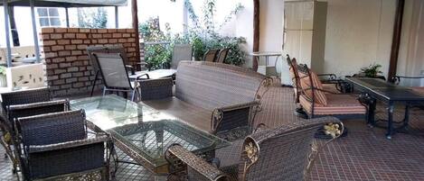 Un espacio al aire libre con mobiliario de mimbre, una mesa con superficie de vidrio y una pared de ladrillo.