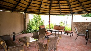 Un patio al aire libre con mobiliario de mimbre, una mesa con cubierta de vidrio y un techo de paja.