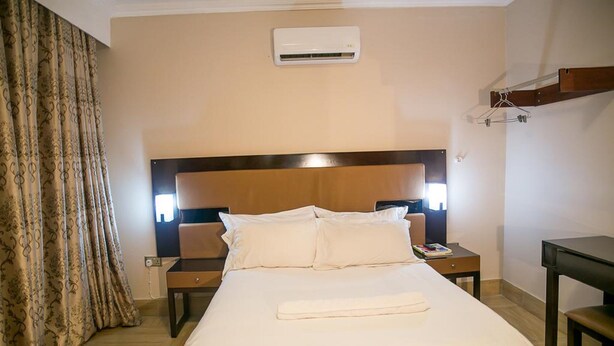Una habitación de hotel con una cama, dos mesitas de noche, un equipo de aire acondicionado y un escritorio.