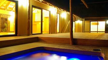A wooden deck with a hot tub, wooden walls, and sliding glass doors leading to a room.