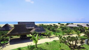 Un complexe hôtelier doté de bâtiments aux toits de chaume, offrant une vue sur la plage et comprenant un jardin bien entretenu.