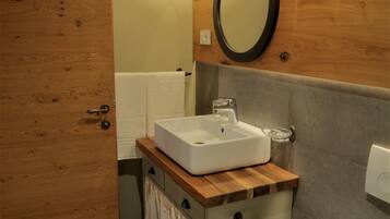 Un baño con puerta de madera, un lavamanos con espejo y un inodoro.