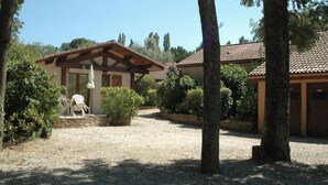 A building with a tiled roof, a covered patio with chairs, and a gravel driveway. - Jardins du Castel Gîtes Annick et J-Paul (Saint-Georges-d'Espéranche)