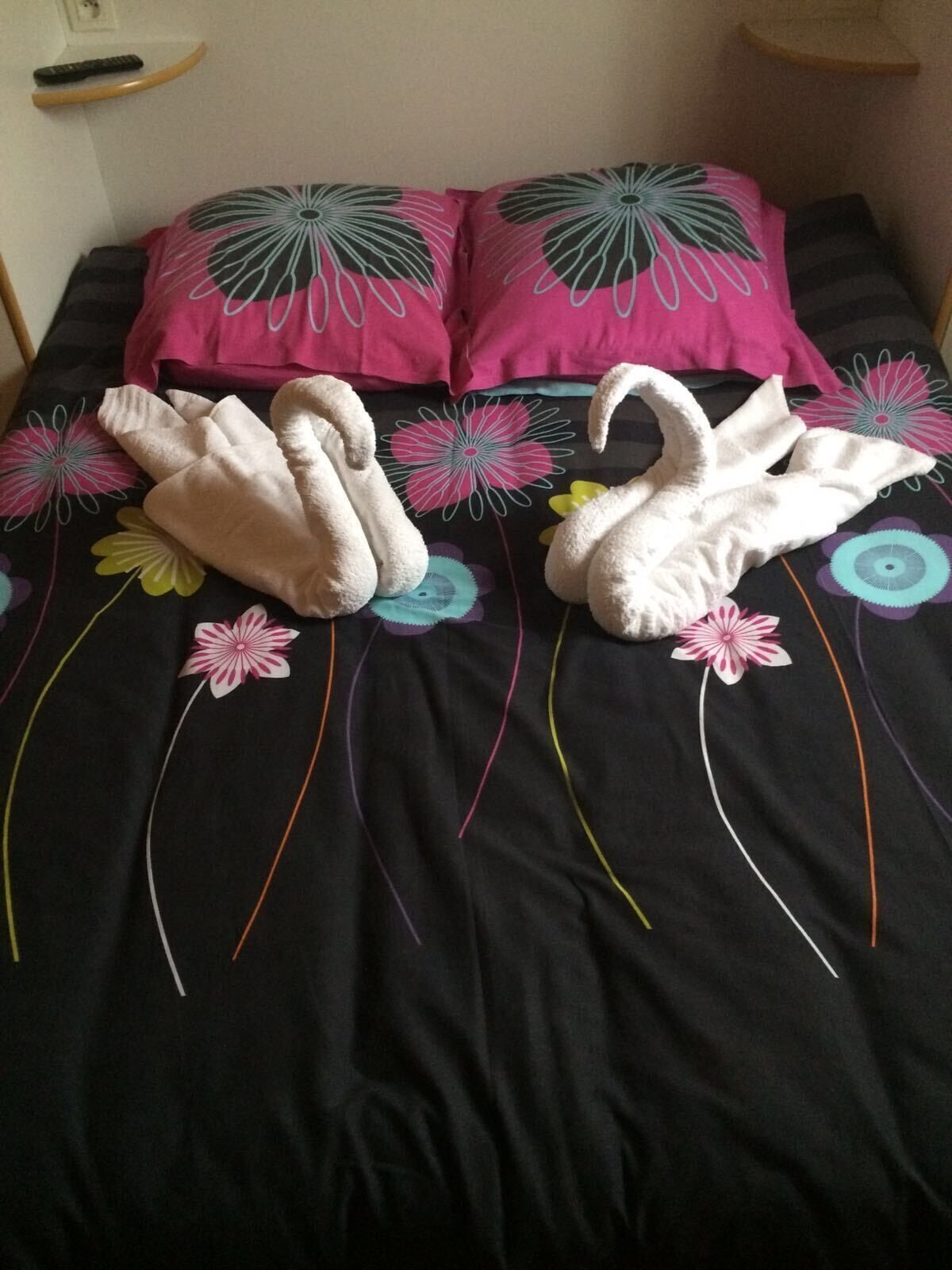 A bed with a black bedspread featuring floral patterns and two white towels shaped like swans.