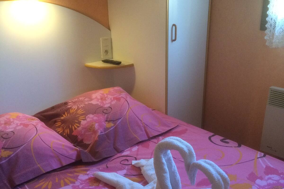 A hotel room with a bed featuring a floral bedspread, a bedside table with a remote control, and a wall-mounted light fixture.