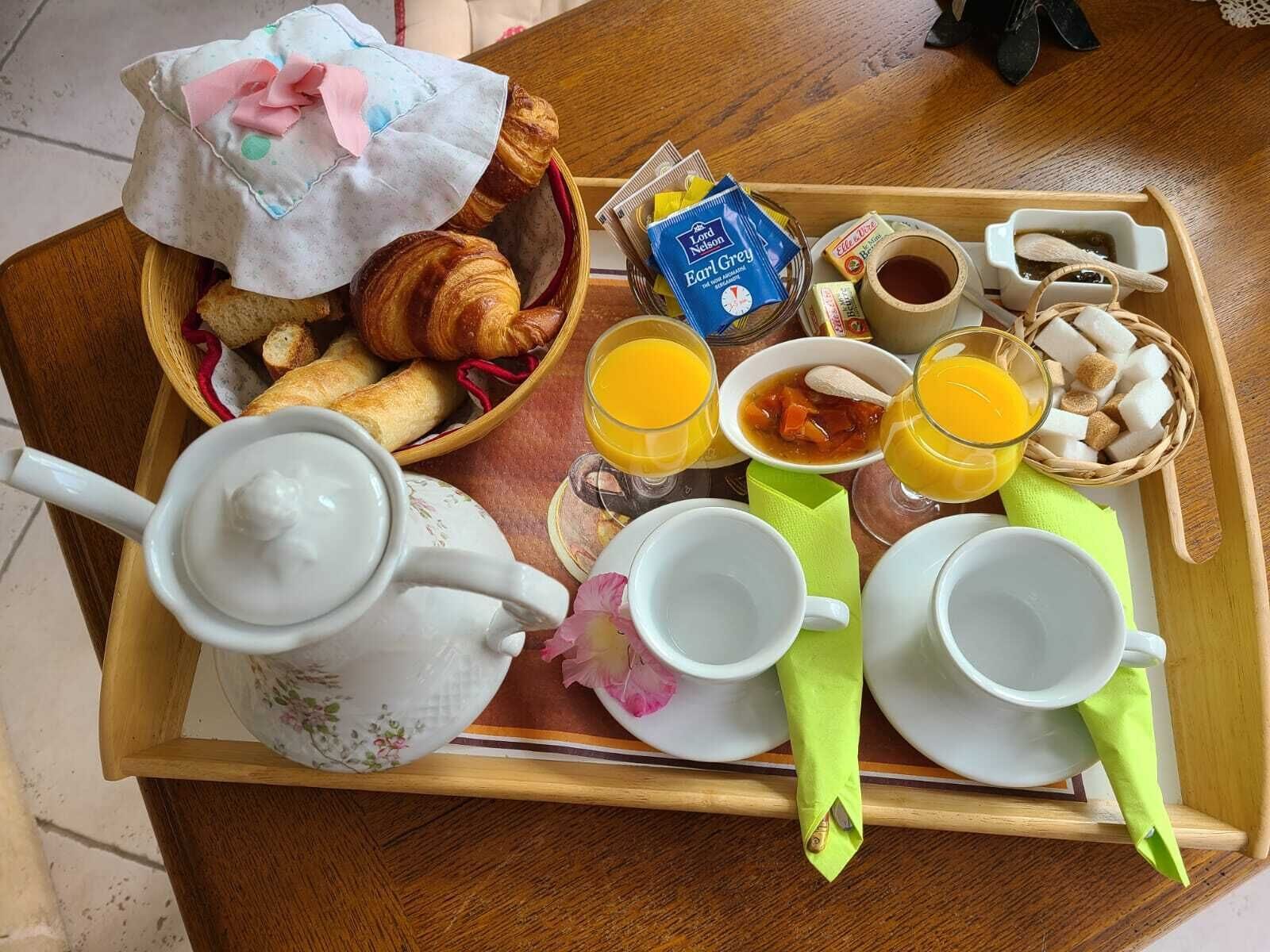A breakfast tray with croissants, Earl Grey tea, orange juice, and sugar cubes.