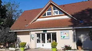 A building with a pitched roof, a front entrance with a door, and a signboard. - Jardins du Castel Gîtes Annick et J-Paul (Saint-Georges-d'Espéranche)