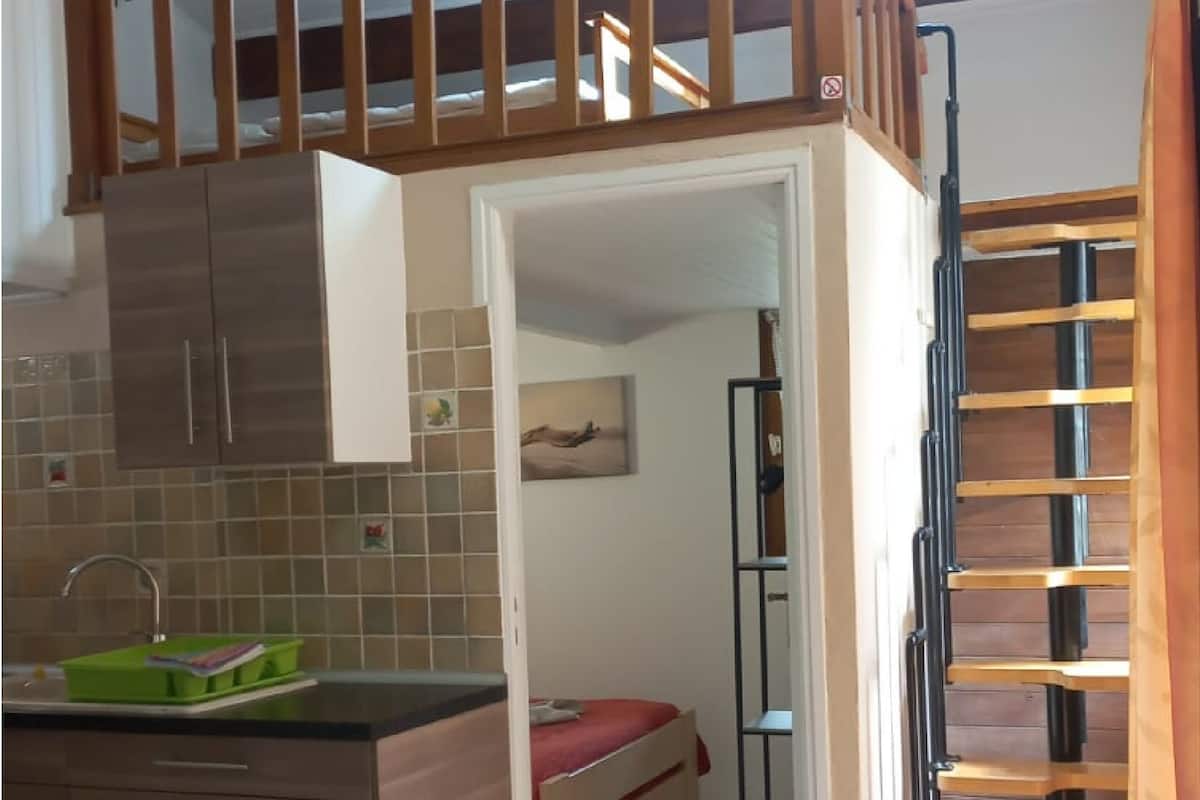 A compact kitchen with a built-in stove, a sink, and a small dining area. A lofted sleeping area is visible above the kitchen.