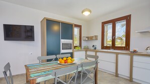 Una cocina moderna con una mesa de comedor preparada para cuatro personas, horno empotrado y ventana con vista a palmeras.