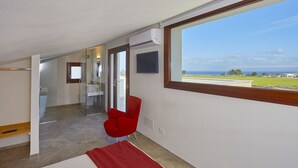 Habitación de hotel moderna con un ventanal grande, una silla roja, un televisor y un baño con cabina de ducha de vidrio.