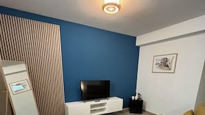 Una sala de estar con una pared azul de acento, un televisor de pantalla plana sobre un mueble blanco, un sofá amarillo y una alfombra marrón.