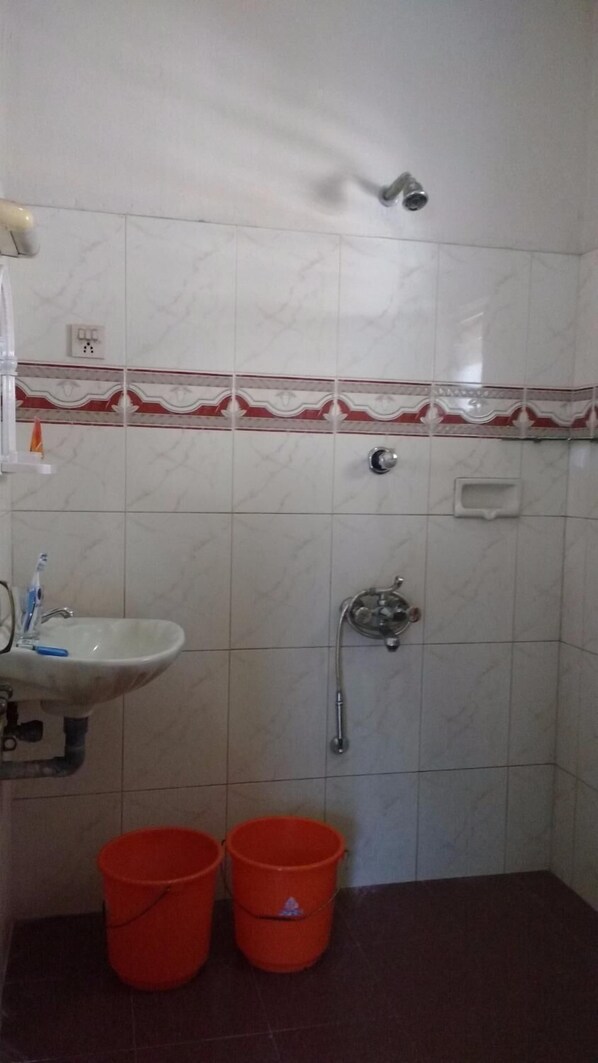 Une salle de bain avec un lavabo, une douche et deux seaux rouges.