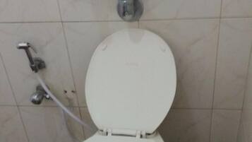 A toilet with a white seat and lid, a visible flush handle, and a wall-mounted flush valve.