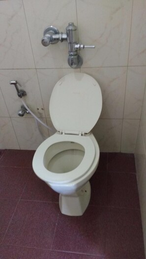 Un inodoro con asiento y tapa blancos, un botón de descarga visible y una válvula de descarga empotrada en la pared.