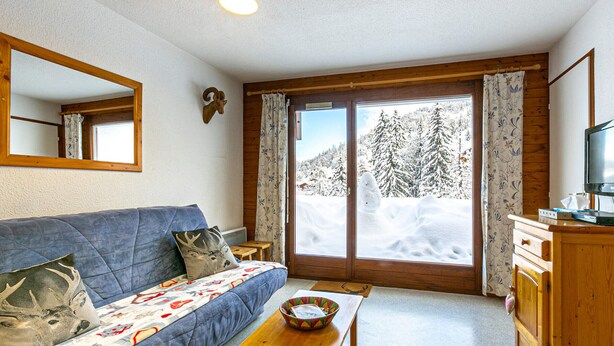 Una sala de estar acogedora con un sofá azul, una mesa de madera y vistas a un bosque nevado a través de un amplio ventanal.