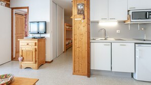 Una cocina compacta con microondas, pileta y muebles de madera. Un televisor está sobre un mueble de madera, y se ve una cama al fondo.