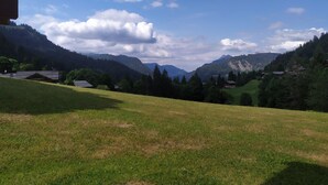 Un campo cubierto de hierba con una cadena montañosa al fondo y algunos edificios.