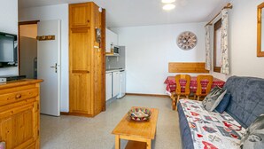 Un espacio habitable compacto con kitchenette, una zona de comedor con mesa y sillas, un sofá y un televisor.