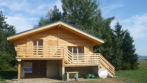 A wooden cabin with a balcony, a staircase leading to the entrance, and a sign indicating a rental service.