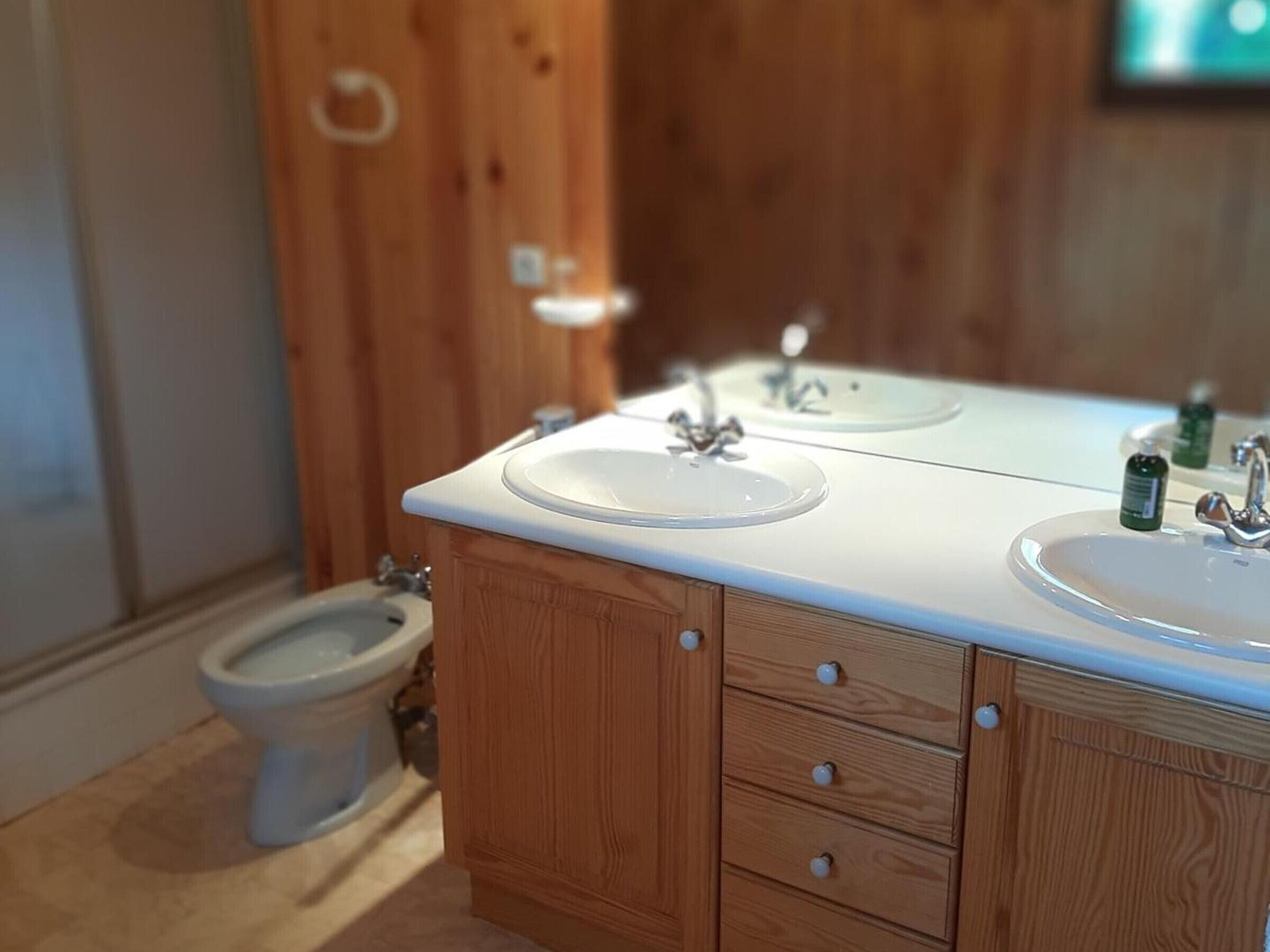 Une salle de bain avec des meubles en bois, deux lavabos, des toilettes et un miroir.