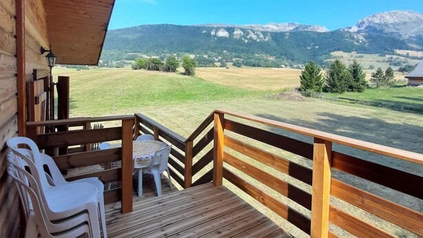 A wooden deck with a table and chairs, overlooking a mountainous landscape.