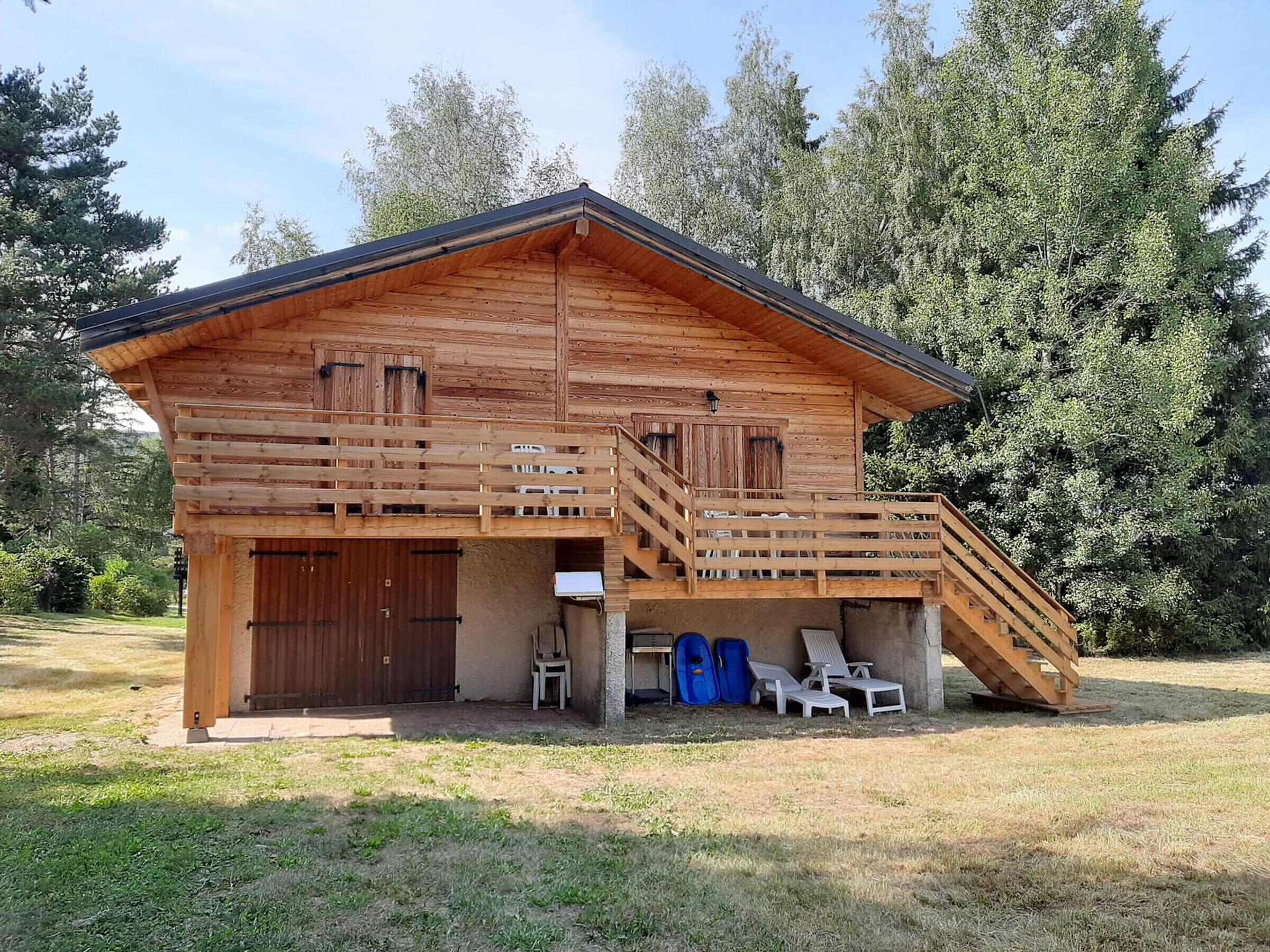 A wooden cabin with a balcony, a covered outdoor seating area, and a staircase leading to the upper level.