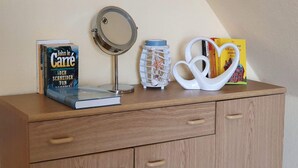 A wooden cabinet with a mirror, a book titled 'John le Carre', a decorative bottle, and a heart-shaped object. - FeWo Düneneck 14- OG (3) (St. Peter-Ording)