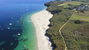 An aerial view of a coastal area with a sandy beach, a road, and scattered boats. - Hôtel Ty Mad (Groix)