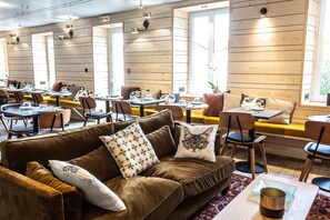 Een gezellig restaurant met houten wanden, verschillende zithoeken, waaronder een bank en tafels, en een bord dat de uitgang aangeeft.