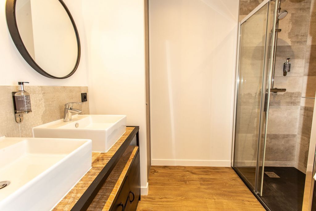 A bathroom with two white sinks, a large mirror, and a glass-enclosed shower.