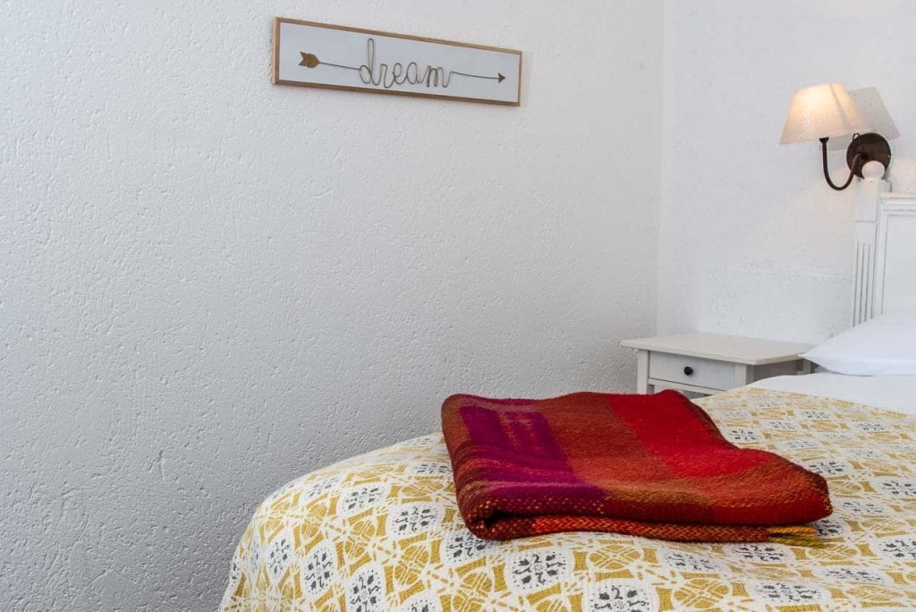 A neatly made bed with a patterned bedspread and a folded blanket on top. A framed sign with the word "dream" hangs on the wall.
