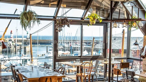 A restaurant with wooden tables and chairs, large windows overlooking a marina with boats. - Hôtel Ty Mad (Groix)