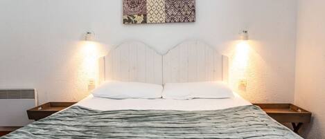 Un dormitorio con una cama, dos mesitas de noche, una lámpara de pared y un adorno en la pared.