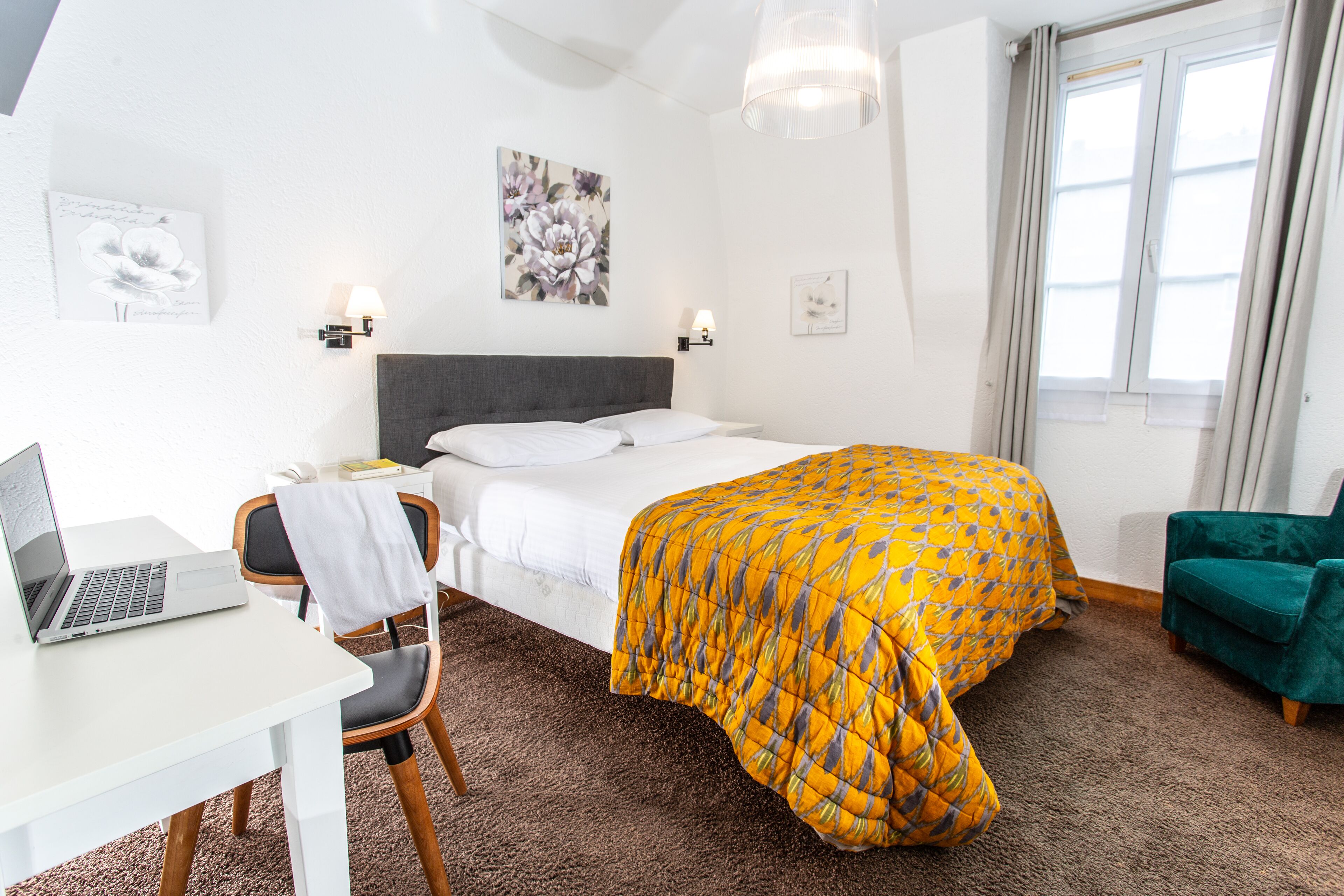 Habitación de hotel con cama, escritorio, laptop, silla y sillón verde.