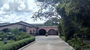 A paved driveway leading to a building with a large arched entrance, surrounded by well-maintained hedges and trees. - Broken Hill Lodge (Kabwe)