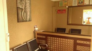 A reception area with a reception desk, chairs, a large framed artwork, and a mirror reflecting a window. - Broken Hill Lodge (Kabwe)