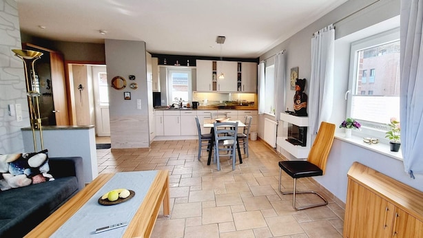 Een moderne keuken met witte kasten, een eethoek met een tafel en stoelen, en een zithoek met een bank en salontafel.