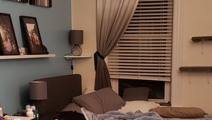 Une chambre à coucher comprenant un lit, une commode, une lampe, une fenêtre avec des stores et un luminaire au plafond.