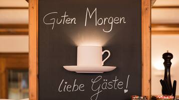 Una pizarra con una taza y un platito y el texto 'Guten Morgen liebe Gäste!'.