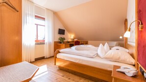 Ein Schlafzimmer mit einem hölzernen Bett, einem Schreibtisch, einem Sessel, einem Fernseher und einem Fenster mit Vorhängen.