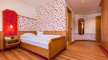 A bedroom with a wooden bed, a red accent wall, a mirror, and a wooden wardrobe.