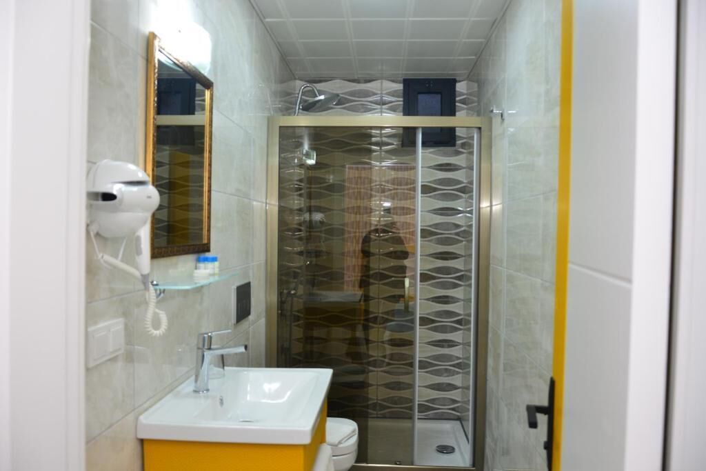 Une salle de bain avec une douche à parois de verre, un lavabo blanc et un sèche-cheveux fixé au mur.
